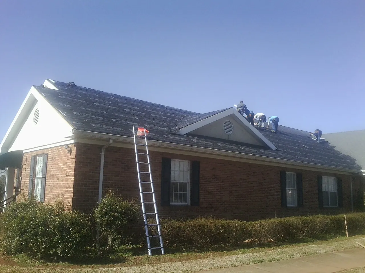 Crew tearing shingles off a brick ranch roof with a ladder set — Metal Roof Repair work by our crew in Paint Lick