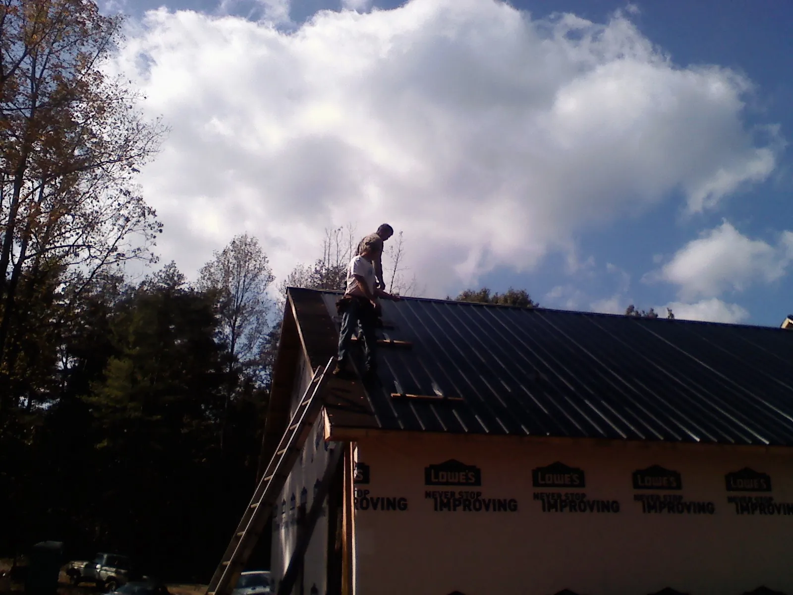 Roofer fastening dark metal panels high against a cloudy sky, from a Roof Inspection job in Paint Lick