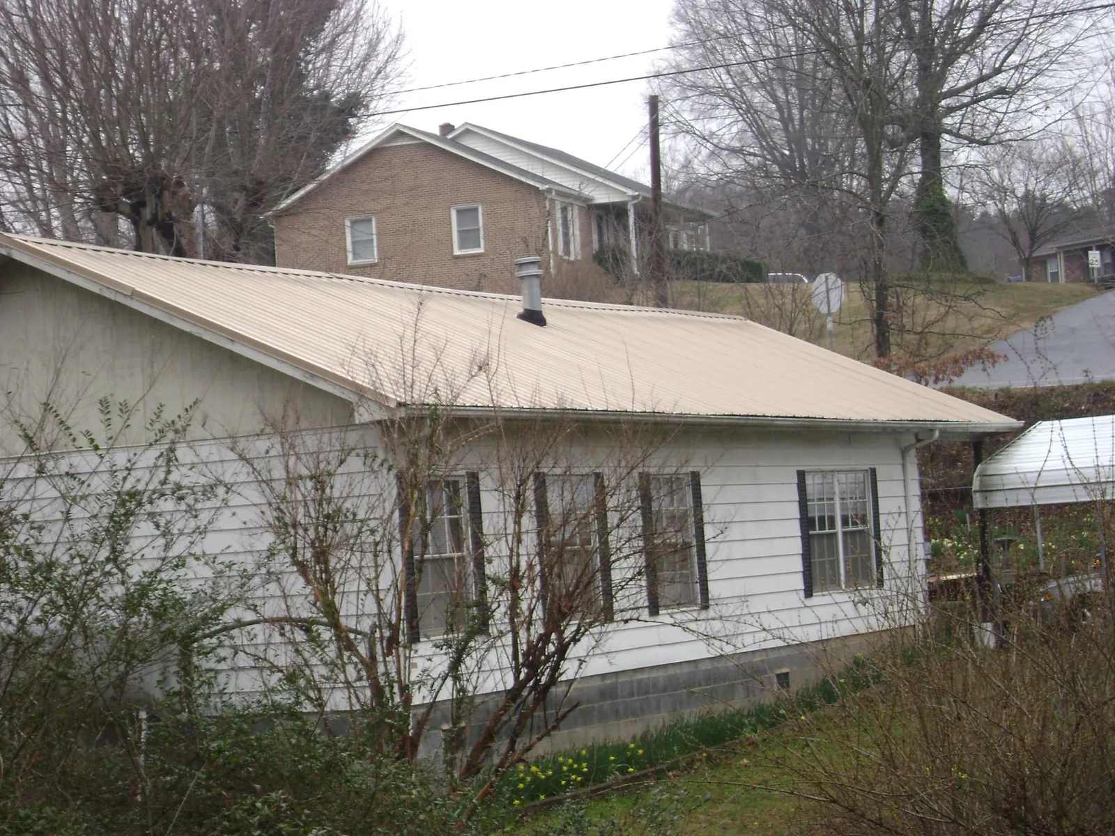 Tan metal roof on a white sided house set into a hillside — Commercial Roofing by Roofing Brothers in Paint Lick